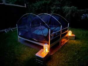 Das Outdoor-Bett SkyHeia nachts in der Dunkelheit zum Draußen Schlafen vorbereitet und gemütlich arrangiert mit Nachttisch und Laterne.