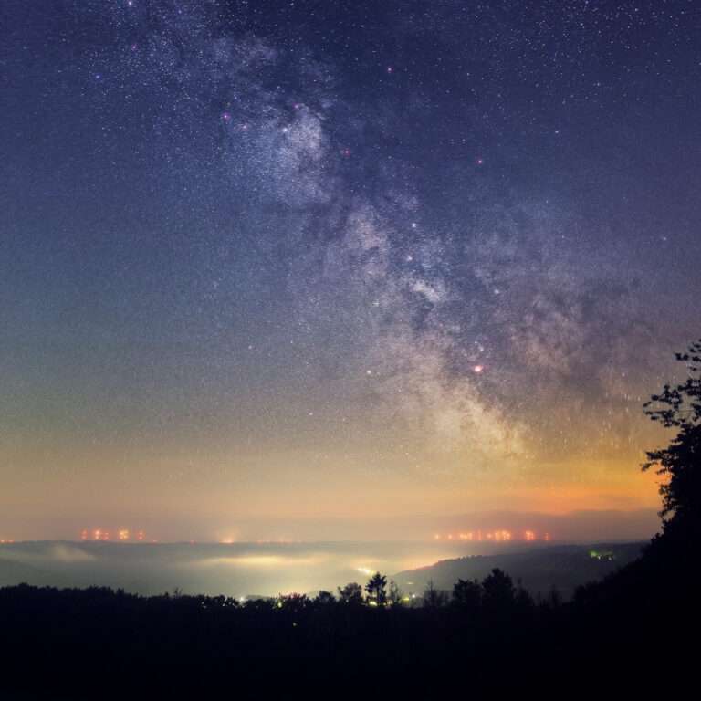 Das Bild zeigt einen üppigen Sternenhimmel über dem Rursee in der Eifel. Von einigen Ortschaft geht eine leichte Lichtverschmutzung aus. Die Sterne sind dennoch sehr gut zu sehen.