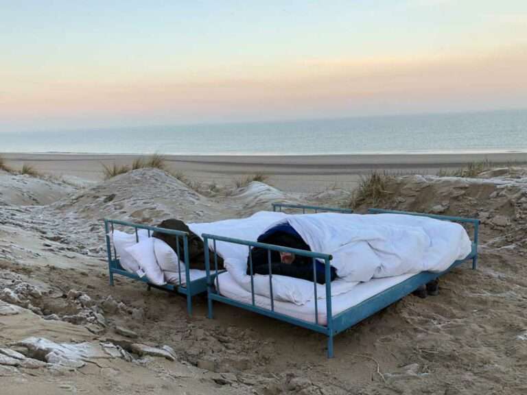 Blog: Schlafen am Strand: Zwei normale Betten (kein spezielles Outdoor-Bett) stehen am Strand an der Nordsee in Wassenaar bei Katwijk. Der Blick geht über die weiße Bettwäsche und das Fußende hinaus auf das Meer. Es ist kurz vor Sonnenaufgang.