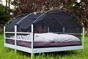 Outdoor bed SkyHeia stands as a double bed (called ZweierHeia) on a meadow. A mosquito net protects the users of the outdoor bed. Cozy looks the bed with its bedding.