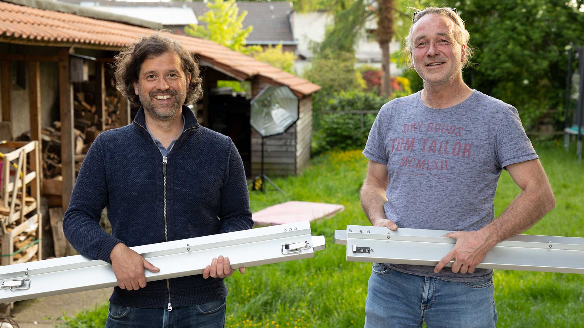 Wir erzählen im Impressum etwas über uns: Das Bild zeigt die beiden Erfinder der SkyHeia, Marco Barooah-Siebertz und Dr. Wolfgang Meschede. Sie halten jeweils einen Seitenholm aus Aluminium der SKYHEIA in den Händen.